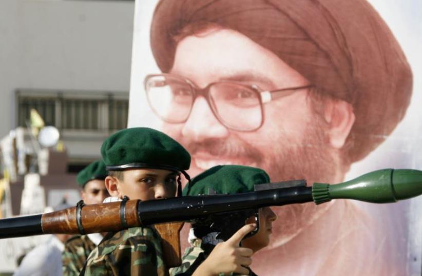 A Hezbollah member carries a mock rocket next to a poster of the group's leader, Hassan Nasrallah (photo credit: REUTERS)