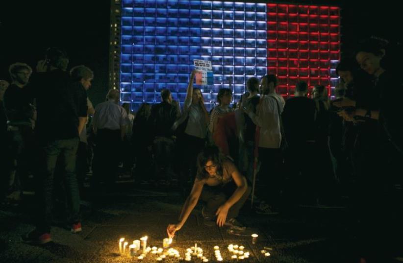 A woman lights candles during a ceremony honoring victims of the attacks in Paris, as the Tel Aviv municipality is lit up in the blue, white and red colors of the French flag, on November 14 (photo credit: REUTERS/BAZ RATNER)