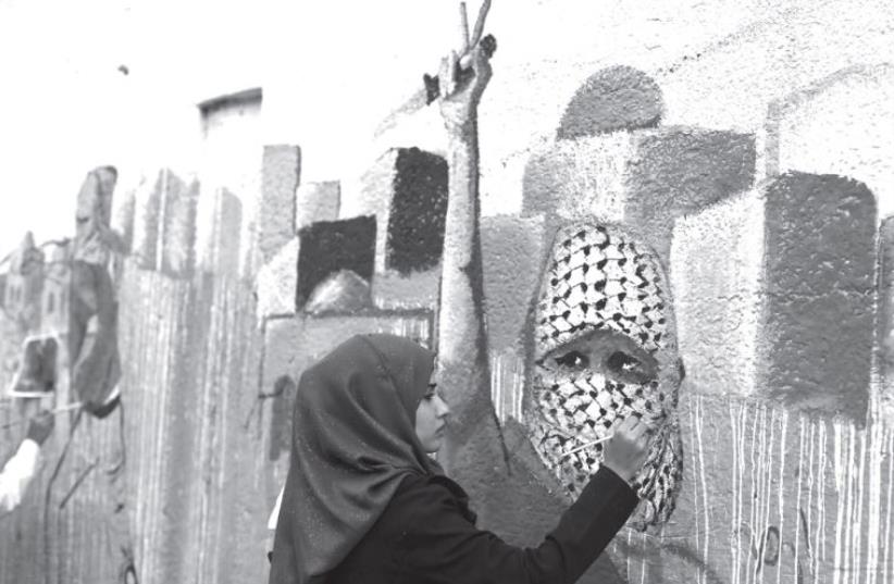 A Palestinian woman paints on a wall (photo credit: REUTERS)