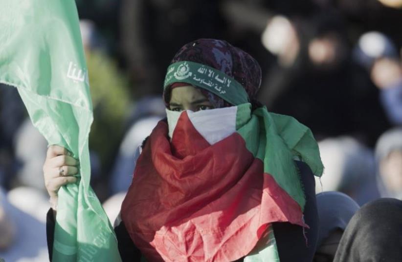 A Palestinian woman covering her face with her national flag takes part in an anti-Israel rally in Gaza City (photo credit: AFP PHOTO)