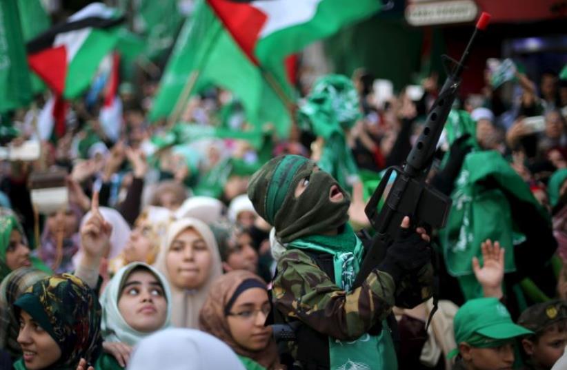 A masked Palestinian boy holds a toy gun as he takes part in a rally marking the 28th anniversary of Hamas' founding (photo credit: REUTERS)