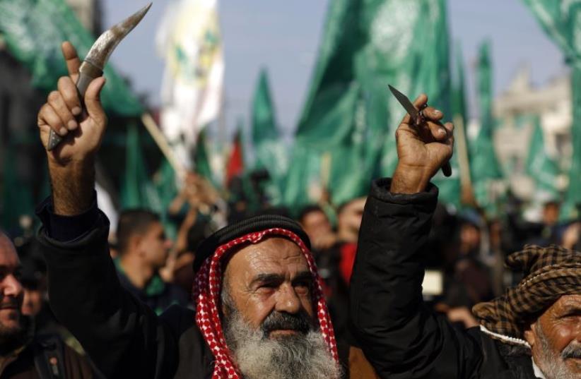 Palestinians carry knives and daggers as they attend a military parade of members of al-Qassam Brigades, the armed wing of the Hamas movement, to mark the 28th anniversary (photo credit: MOHAMMED ABED / AFP)