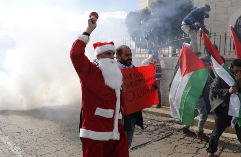 A Palestinian protester dressed in a Santa Claus costume rings a bell in front of tear gas fired by Israeli troops during a demonstration against the settlements  (photo credit: REUTERS)