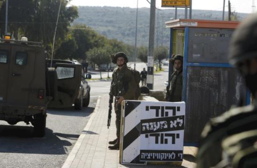 IDF SOLDIERS stand guard next to a poster which reads in Hebrew, ‘A Jew doesn’t torture a Jew. Enough with the inquisition,’ at the entrance to Ariel (photo credit: REUTERS)