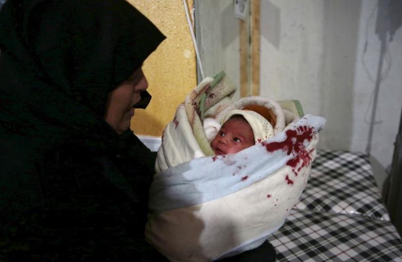 A woman carries an injured baby born inside a field hospital after what activists said were air and missile strikes in the Douma neighborhood of Damascus (photo credit: REUTERS)