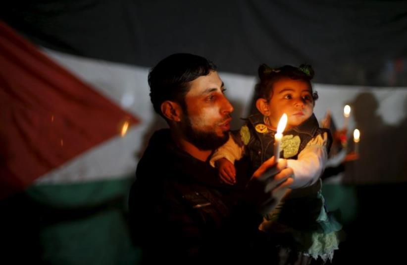 A Palestinian man and his daughter hold candles during a rally to pay tribute to Palestinians who organizers said were killed recently by Israeli troops (photo credit: REUTERS)