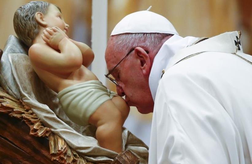 Pope Francis kisses a statue of baby Jesus as he leads the Christmas night Mass in Saint Peter's Basilica at the Vatican  (photo credit: REUTERS)