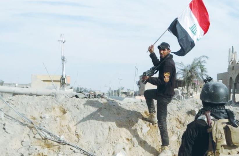 A MEMBER of Iraq’s security forces holds an Iraqi flag in Ramadi on Sunday (photo credit: REUTERS)