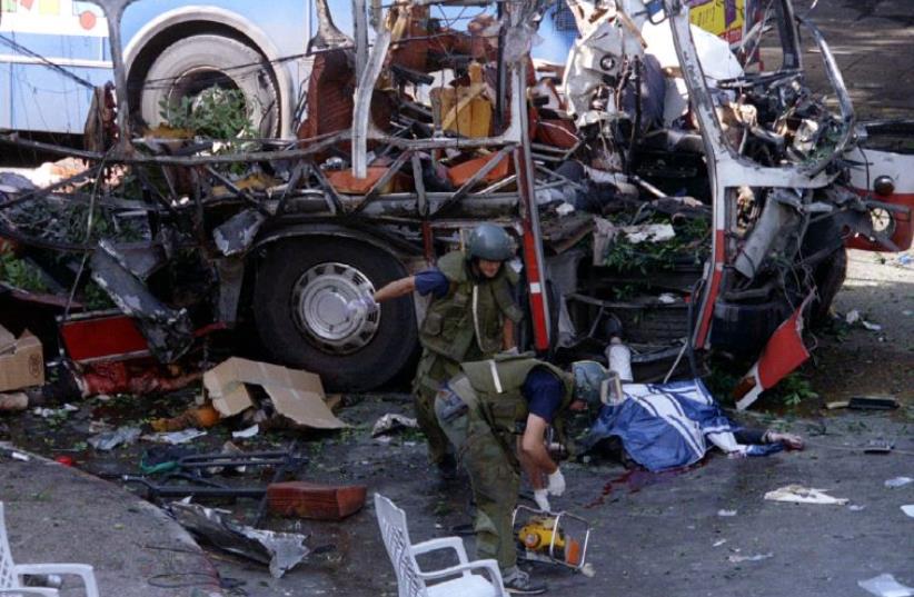 Police sappers looking for additional bombs prepare their equipment next to the covered body, lying on the street by the bus door, of one of the 22 victims from the large explosion that ripped apart a Tel Aviv bus (photo credit: REUTERS)