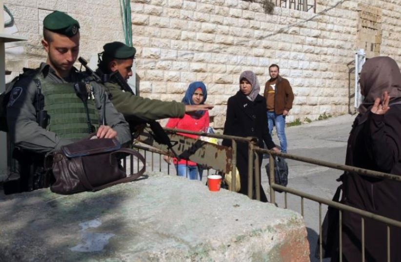 Border Police officers stop Palestinian women to check their belongings at a checkpoint in Hebron (photo credit: AFP PHOTO)