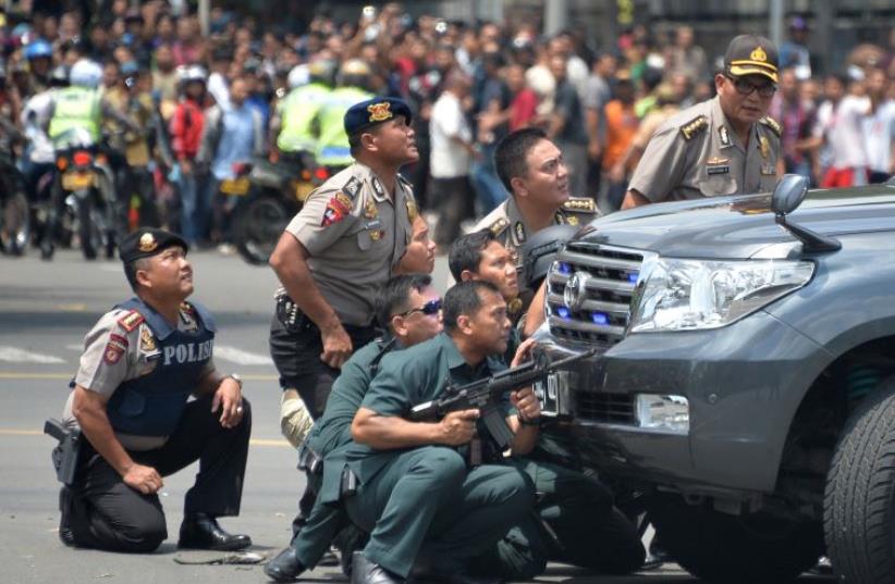 Indonesian police take position behind a vehicle as they pursue suspects after a series of blasts hit the Indonesia capital Jakarta on January 14, 2016 (photo credit: AFP PHOTO/BAY ISMOYO)