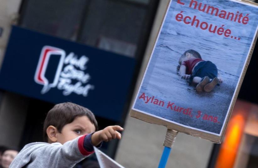 A young boy points at the picture of Aylan, a Syrian toddler whose body washed up on a Turkish beach, during a demonstration in Paris (photo credit: REUTERS)