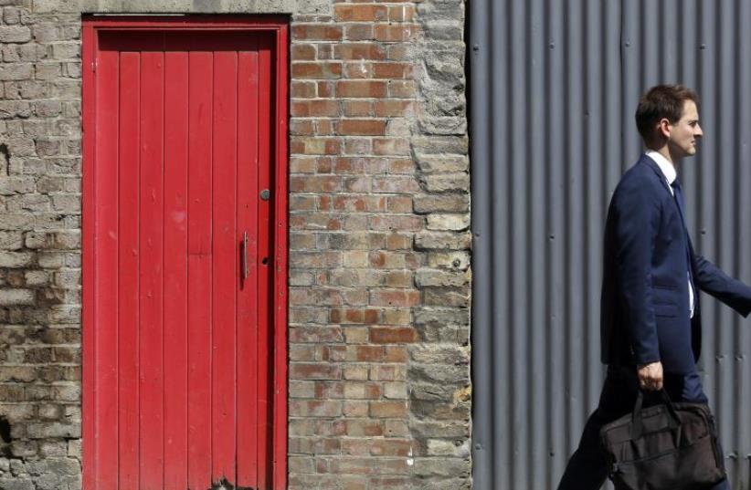 A man passes a red door and corrugated iron in central London  (photo credit: REUTERS)