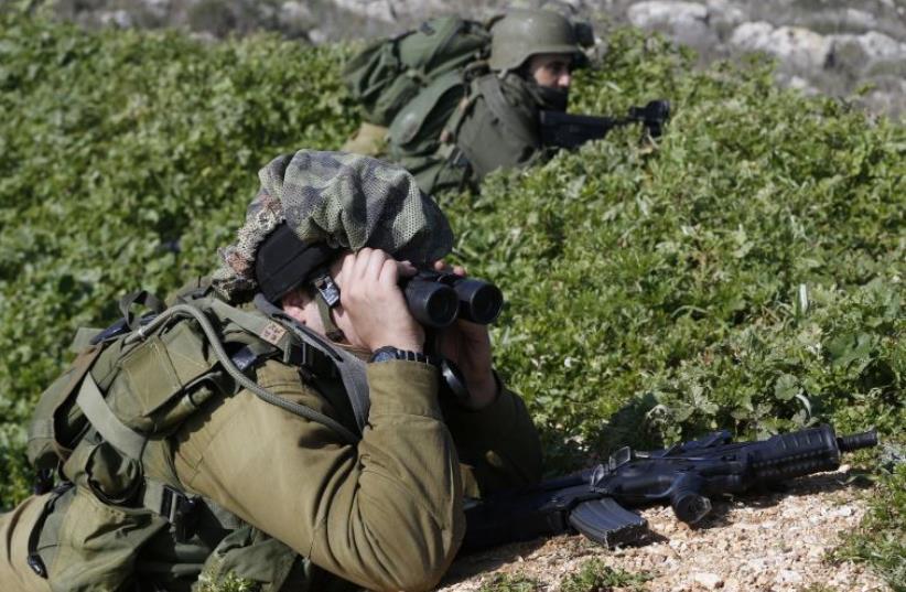 An Israeli soldier looks through binoculars towards the border with Lebanon (photo credit: REUTERS)