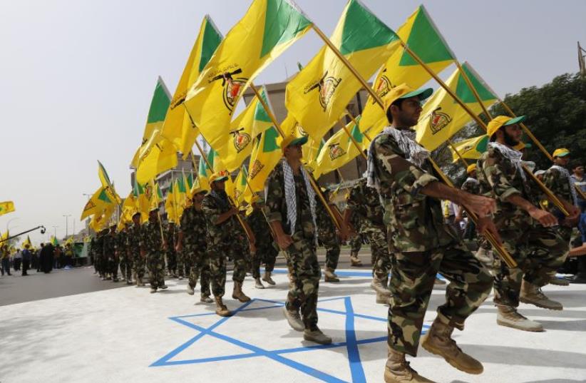 Iraqi Shi'ite Muslim men from the Iranian-backed group Kataib Hezbollah wave the party's flags as they walk along a street painted in the colours of the Israeli flag during a parade marking the annual Quds Day (photo credit: REUTERS)