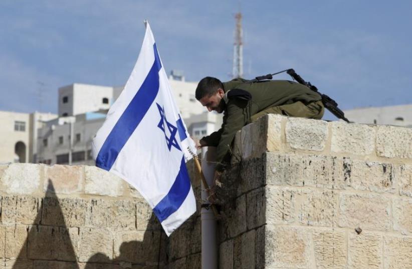 An Israeli soldier removes the Israeli flag from a house as Israeli troops forcibly remove Jewish settlers from homes in Hebron (photo credit: REUTERS)