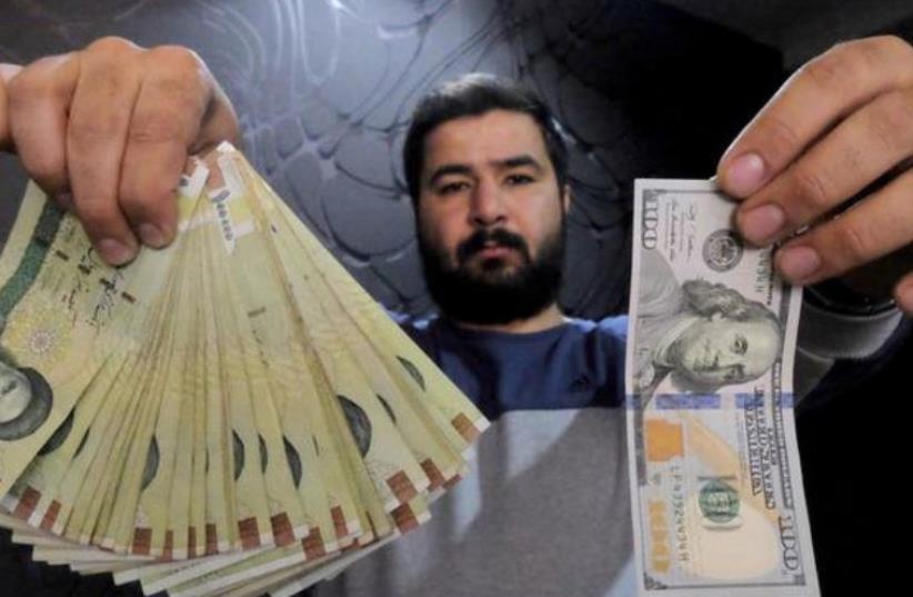 A money changer poses for the camera with a U.S dollar (R) and the amount being given when converting it into Iranian rials (L), at a currency exchange shop in Tehran's business district, Iran, January 20, 2016. (photo credit: REUTERS)