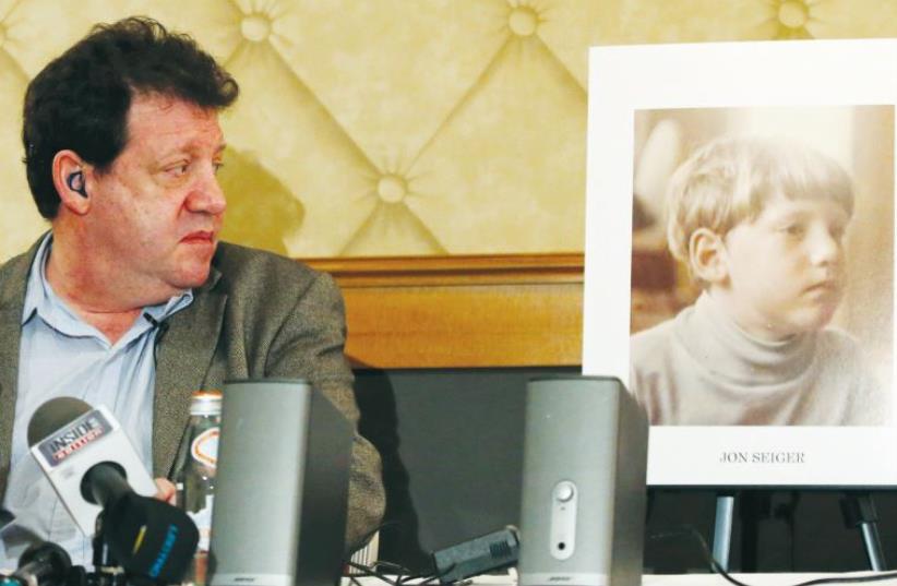 Jon Sieger, a former student at Horace Mann School, who has alleged sexual abuse during his time there, sits beside a picture of himself during a news conference in New York in 2013 (photo credit: REUTERS)