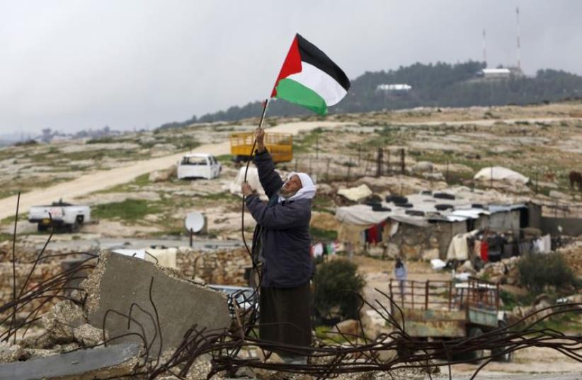 A Palestinian man hangs a Palestinian flag atop the ruins of a mosque, during a snow storm in West Bank village of Mufagara (photo credit: REUTERS)