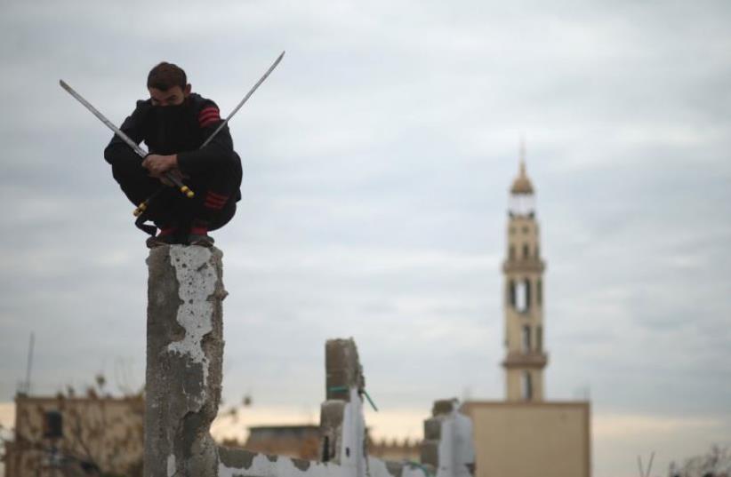 A Palestinian youth holds swords as he demonstrates his ninja-style skills for a photographer at the ruins of a house that was destroyed in the 2014 war (photo credit: REUTERS)