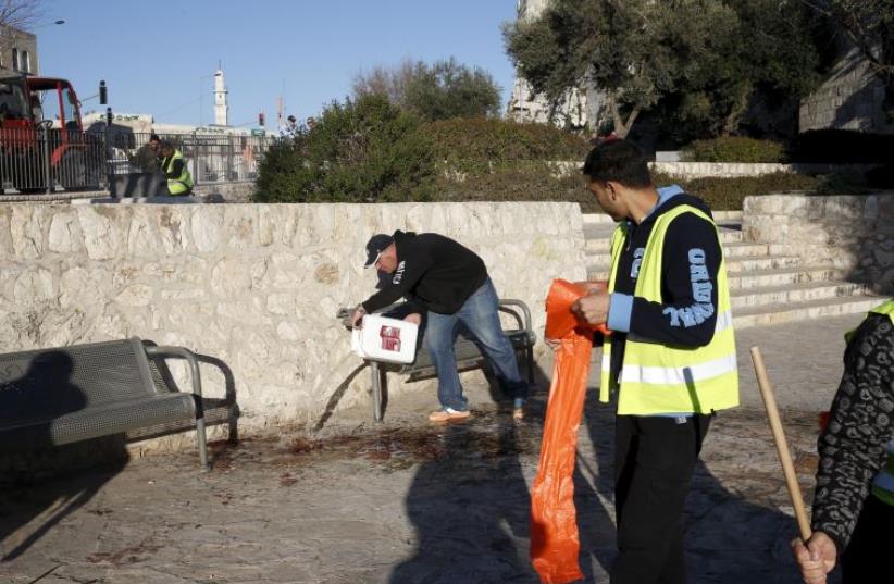 A man pours water over blood stains at the scene where 3 Palestinian terrorists were shot dead by Israeli police after carrying out a shooting and stabbing attack outside Damascus Gate to Jerusalem's Old City February 3, 2016. (photo credit: REUTERS)