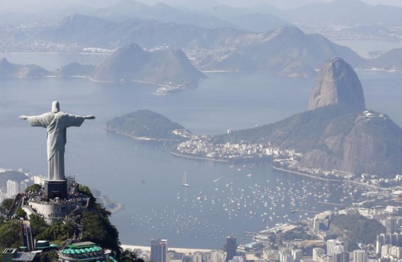 Tourists visit the Christ the Redeemer statue with Sugarloaf Mountain (R) in the distance in Rio de Janeiro (photo credit: REUTERS)