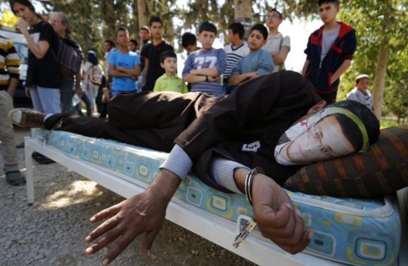 A Palestinian man in Ramallah lies on a bed wears a face covering depicting hunger striking Palestinian journalist Mohammed al-Qiq (photo credit: AFP PHOTO)