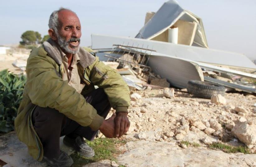 A Palestinian man sits next to the remains of his dwelling after it was demolished by Israeli forces (photo credit: REUTERS)