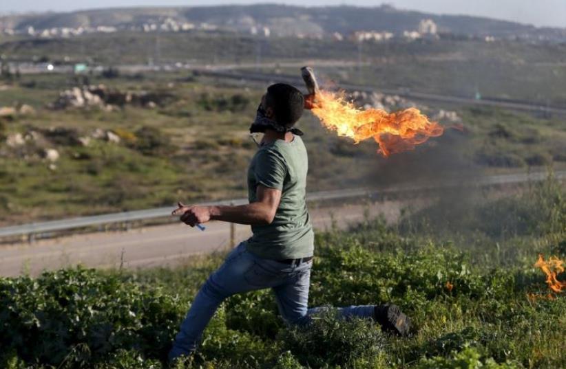 A Palestinian protester hurls a Molotov cocktail towards Israeli troops during clashes near Israel's Ofer Prison near Ramallah (photo credit: REUTERS)