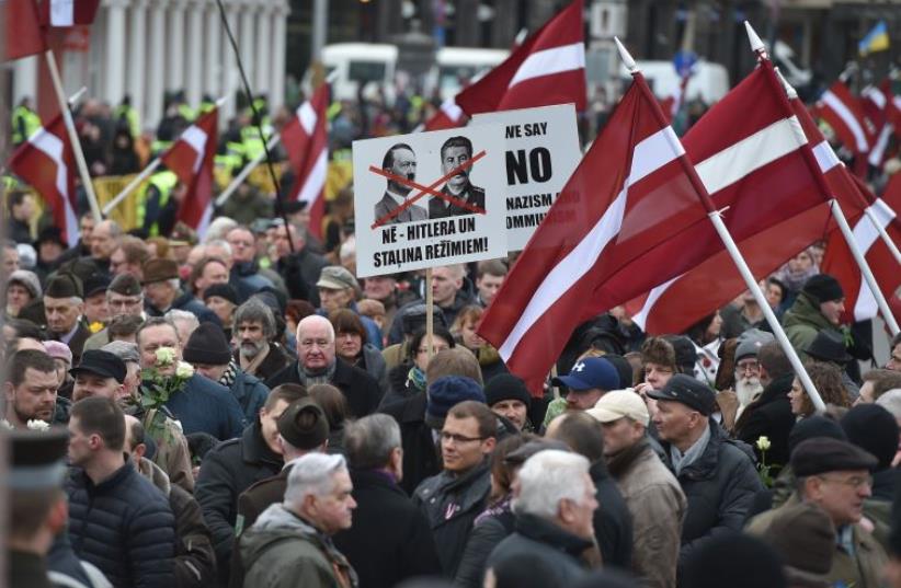 Veterans of the Latvian Legion, a force that was commanded by the German Nazi Waffen SS during WWII, and their sympathizers carry flags and posters as they walk to the Monument of Freedom in Riga, Latvia on March 16, 2016 (photo credit: ILMARS ZNOTINS/AFP)