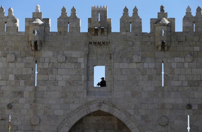 A Border Policeman holds his weapon as he guards the area from above while his comrades patrol at Damascus Gate in Jerusalem's Old City (photo credit: REUTERS)