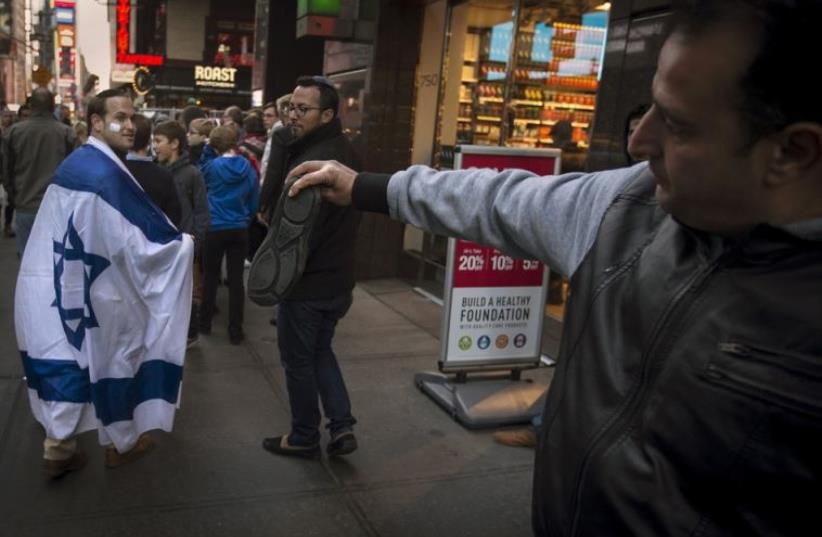 A man, draped in an Israeli flag, reacts while walking past a pro-Palestinian demonstrator who threatens to throw a shoe at him in New York (photo credit: REUTERS)