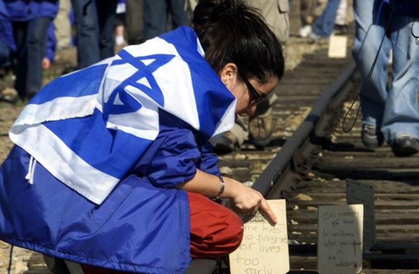 A Jewish girl places a wooden board on railway tracks to commemorate her relatives killed at the former Nazi death camp in Auschwitz-Birkenau (photo credit: REUTERS)