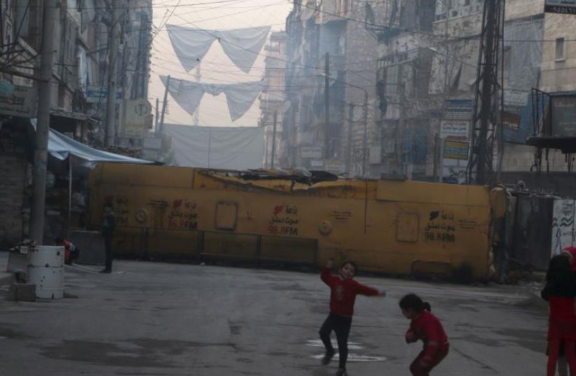 Children play near a bus barricading a street, which serves as protection from snipers loyal to Syria's President Bashar Assad, in Aleppo's rebel-controlled Bustan al-Qasr neighborhood, Syria April 6, 2016.  (photo credit: REUTERS)