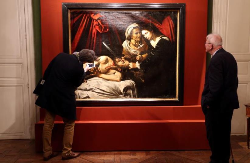 Visitors looks at a painting entitled "Judith Beheading Holofernes" during its presentation in Paris, France, April 12, 2016, that might have been painted by Italian master Caravaggio (1571-1610) and was discovered in an attic in Toulouse and could be worth more than 100 million euros.  (photo credit: REUTERS)