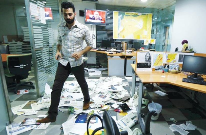 An employee walks on newspapers after protesters attacked the office of Saudi-owned newspaper ‘Asharq al-Awsat’ in Beirut, in this April 1 file photo (photo credit: REUTERS)