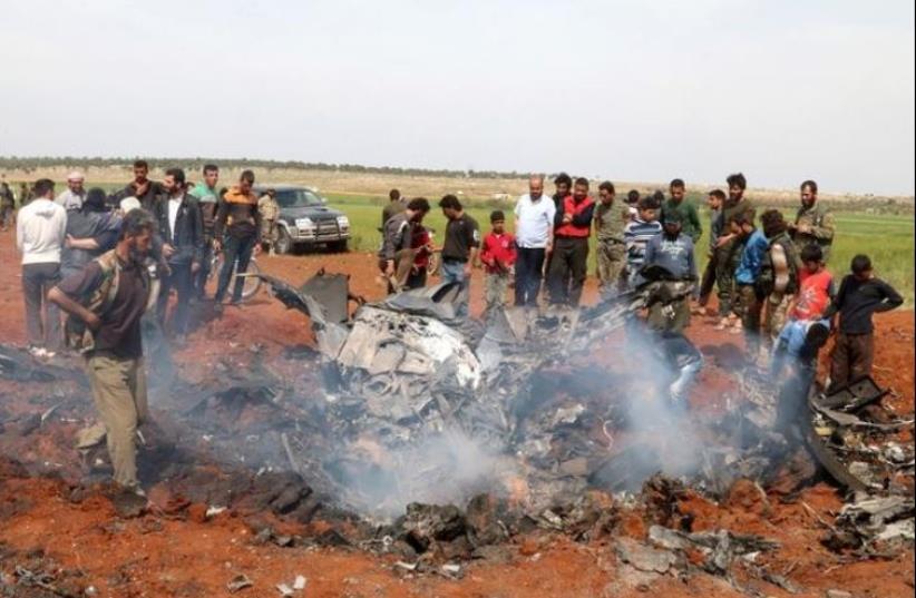 Rebel fighters and civilians gather around the wreckage of a Syrian warplane that was shot down. (photo credit: REUTERS)