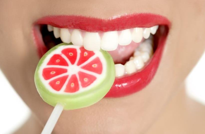 A woman with perfect teeth chews on a lollipop (photo credit: INGIMAGE)
