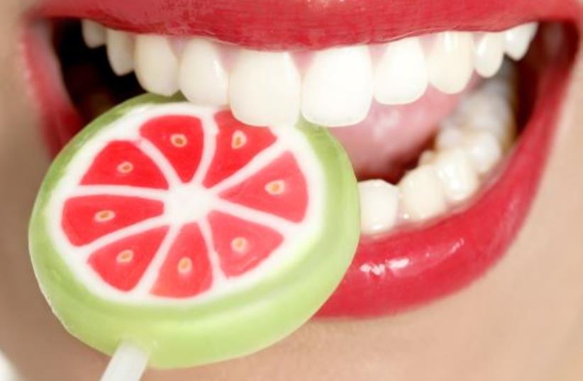 A woman with perfect teeth chews on a lollipop (photo credit: INGIMAGE)