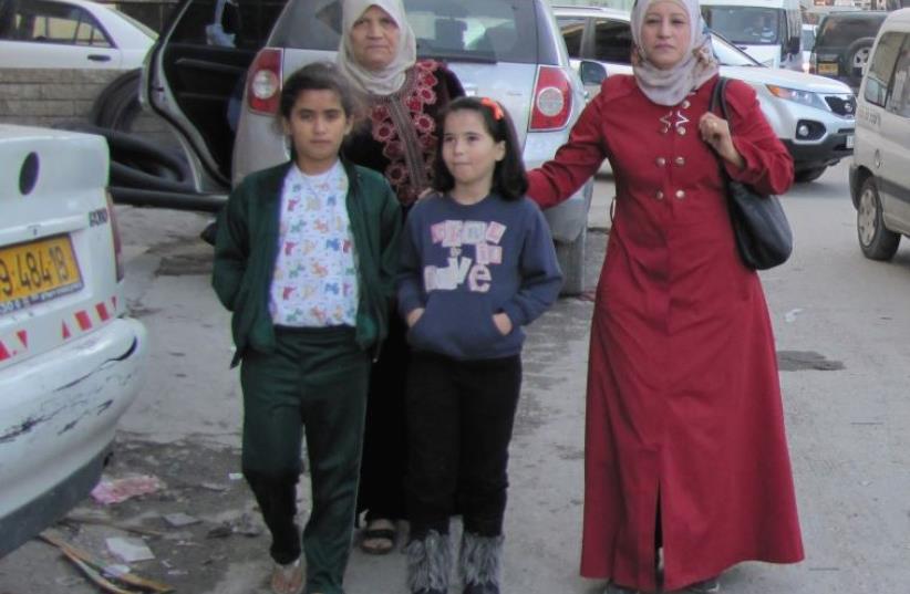 Muna Zatari (in red) steers her nieces through a street teeming with garbage and cars in the Shuafat Refugee Camp (photo credit: JUDITH SUDILOVSKY)