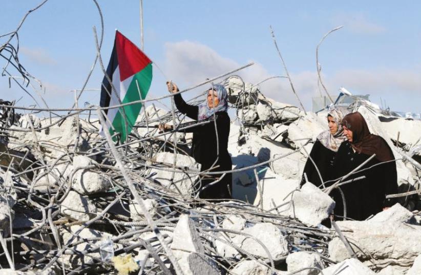 The mother of Palestinian assailant Murad Adais stands with a flag in the rubble of the family’s home in Yatta after it was demolished by the IDF (photo credit: REUTERS)