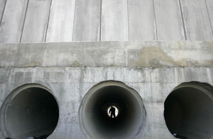 A Palestinian walks through a water pipe underneath the controversial Israeli barrier in al-Ram, on the edge of Jerusalem [File] (photo credit: REUTERS)