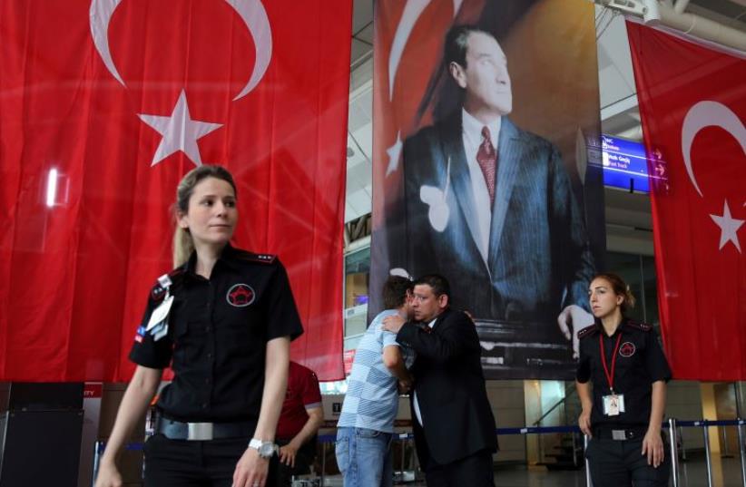 Men greet each other in front of Turkish flag and picture of modern Turkey's founder Mustafa Kemal Ataturk at Istanbul Ataturk airport, Turkey, following yesterday's blast June 29, 2016.  (photo credit: REUTERS)