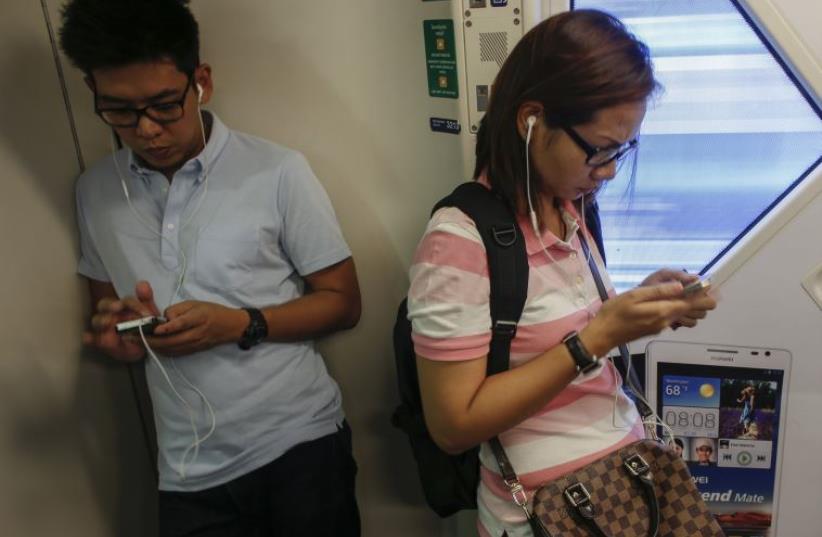 Passengers use their mobile phones on a skytrain in Bangkok June 20, 2014. (photo credit: REUTERS)