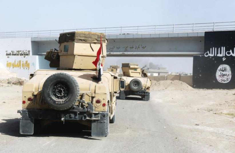 Iraqi military vehicles pass by the flag of Islamic State militants in Falluja, Iraq (photo credit: REUTERS)