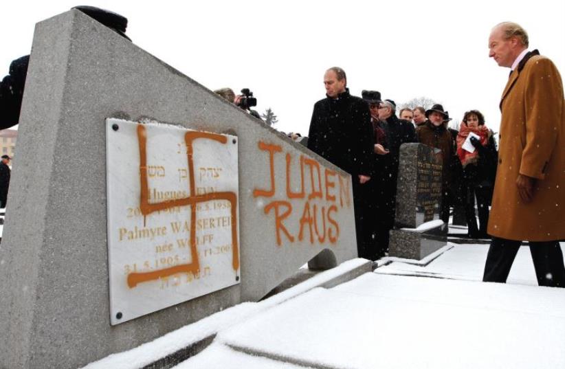 FRANCE’S THEN interior minister Brice Hortefeux walks next to a tombstone desecrated by vandals with a Nazi swastika and the slogan ‘Jews out’ in the Jewish Cemetery of Cronenbourg near Strasbourg in 2010 (photo credit: REUTERS)