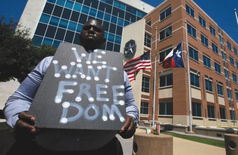 A MAN holds a sign at police headquarters earlier this week following the multiple police shootings in Dallas, Texas. (photo credit: CARLO ALLEGRI/REUTERS)