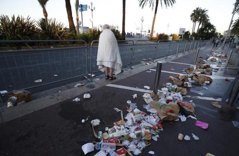 A man walks through debris scatterd on the street the day after a truck ran into a crowd at high speed killing scores celebrating the Bastille Day July 14 national holiday on the Promenade des Anglais in Nice, France, July 15, 2016. (photo credit: REUTERS/ERIC GAILLARD)