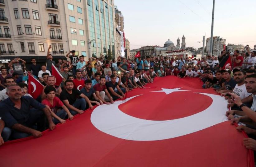 Supporters of Turkish President Tayyip Erdogan wave a huge national flag as they gather at Taksim Square in central Istanbul, Turkey, July 16, 2016. (photo credit: REUTERS)