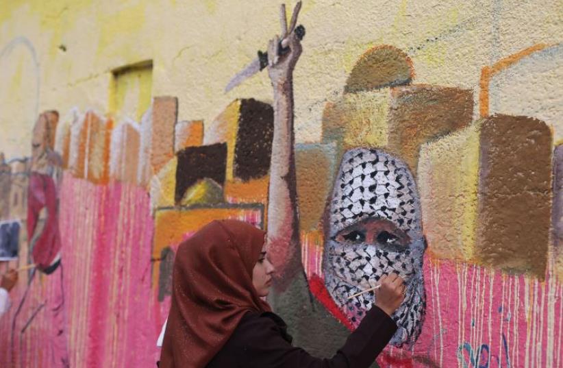 A PALESTINIAN woman paints a mural in support of Palestinians committing stabbing attacks against Israelis, in the southern Gaza Strip in November (photo credit: IBRAHEEM ABU MUSTAFA / REUTERS)